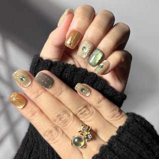 Hand showcasing EyeCandys Sun Spell cat-eye press on nails in nude, amber, and green tones.