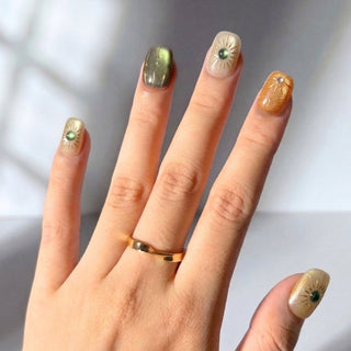 Hand wearing EyeCandys Sun Spell press on nails featuring a cat-eye design in nude, amber, and green with sun-inspired details.