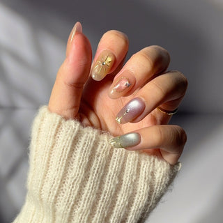 Hand showcasing EyeCandys Star Script press on nails featuring warm peach and gold cat-eye glow with metallic celestial motifs.