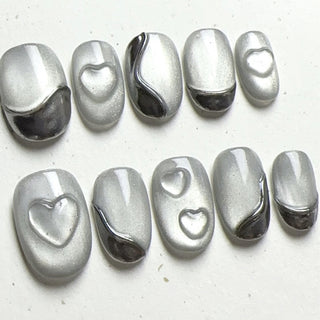 Close-up of EyeCandys Soft Signals press on nails on a white background featuring grey cat-eye base with subtle magnetic glow, silver chrome accents, and sculpted heart details.