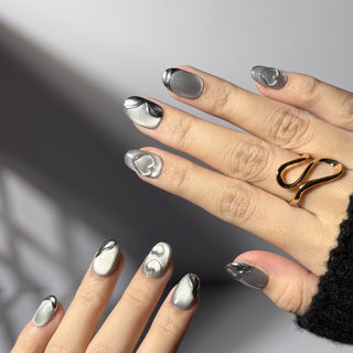 Hand wearing EyeCandys Soft Signals press on nails with grey cat-eye base, magnetic glow, silver chrome accents, and subtle heart details.