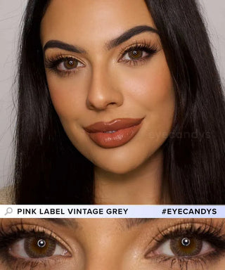 A woman with long dark hair wears makeup and EyeCandys Pink Label Vintage Grey contact lenses. She's smiling, and a close-up highlights her brown eyes with the dolly look. Text says "Pink Label Vintage Grey #EYECANDYS.