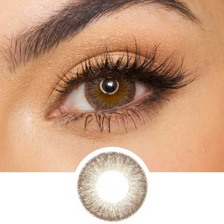 Close-up of a brown eye with long lashes and golden-beige makeup. Below the eye is EyeCandys Pink Label Vintage Grey contact lens, highlighting its intricate pattern and color.