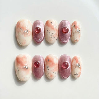 Short oval press on nails EyeCandys Raspberry Ripple with peach cream marble design, cat eye nails, silver foil flakes, and pearl rhinestone details.