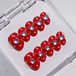 EyeCandys Spot the Difference Press-On Nails feature red nails with white polka dots and metallic silver heart and star designs, styled like a salon gel manicure, all neatly packaged in a clear plastic case.