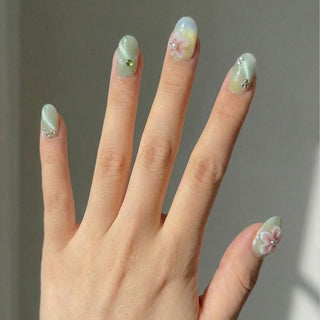 Hand wearing EyeCandys Spring Fling press on nails featuring sage green to cream gradient with 3D cherry blossoms and crystal accents.