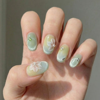 Close up hand showcasing EyeCandys Spring Fling press on nails with soft sage ombre, cherry blossom nail art, and shimmering crystals.