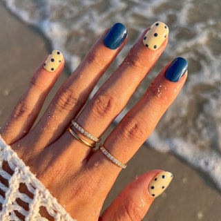 Hand wearing EyeCandys Sunny Side Up press on nails featuring butter yellow nails with navy polka dots and solid navy color block nails.