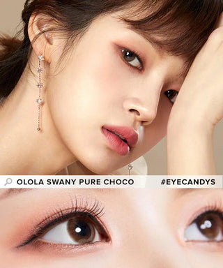 A close-up of a woman with peach makeup, dangling earrings, and Olola Swany Pure Choco contacts. An enlarged view below highlights the brown lenses by Olola. Text: "Olola Swany Pure Choco #EYECANDYS".