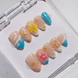EyeCandys Tahiti Feeling Press-On Nails offer reusable beach-themed nails with blue tips, 3D yellow and pink flowers, white and gold seashells, star accents, and pearls in a clear case for a salon-quality gel manicure look.