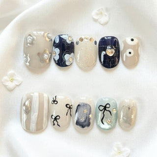 EyeCandys All Tied Up press on nails with greige base, gold heart charm, pearl flower cluster, ribbon bow designs, and mint shimmer accents.