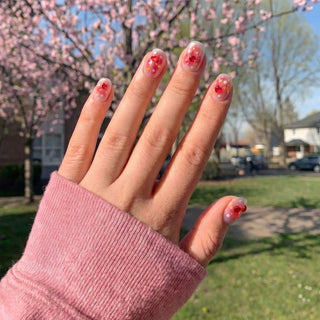 Hand wearing EyeCandys Catching Feelings press on nails featuring sheer peach jelly nails with embedded heart sequins and glitter confetti.