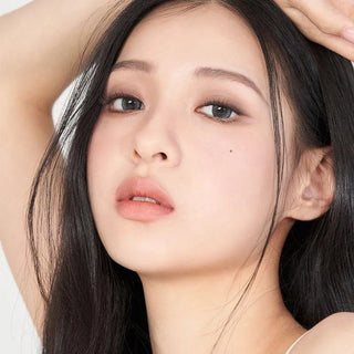 A young woman with long dark hair and smooth, fair skin poses serenely, her beauty mark visible. Her natural look is highlighted by Gemhour Demeter 1-Day 13.0 Ocean Blue color contacts (10pk) from Gemhour against a light background.
