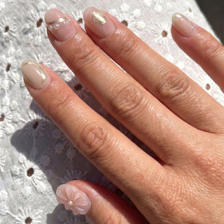 Hand wearing reusable EyeCandys En Rose press on nails featuring blush pink floral design, pearl center flower, and elegant gold detailing.