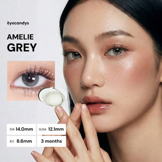 A woman with flawless makeup wears EyeCandys Amelie Earl Grey lenses for a natural look. Inset shows a close-up of her eye and lens design. Text: DIA 14.0mm, G.DIA 12.1mm, B.C 8.6mm, 3 months. Brand: EyeCandys.