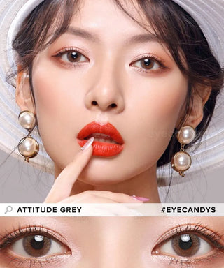A woman with wavy dark hair wears a white hat, pearl earrings, and bold red lipstick. In a close-up below, her eyes feature EyeCandys Attitude Glitter Grey contacts. Text reads "Attitude Glitter Grey" and "#EYECANDYS.