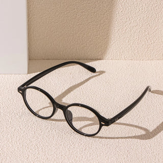 A pair of EyeCandys Chase Round Oval Glasses with clear lenses rests on a textured beige surface, casting soft shadows against a light-colored wall in the background.