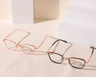 Two pairs of EyeCandys Kaylee Cat Eye glasses with thin metal frames—one in rose gold, the other in rose gold and black—rest on a textured beige surface, highlighted by white geometric blocks for a chic, modern look.
