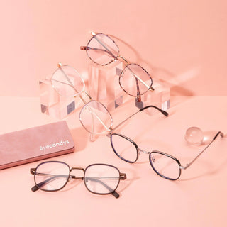 Four pairs of fashion glasses, including metal frames and EyeCandys' Stunner Square, are displayed on clear acrylic stands against a pink background. A pink EyeCandys case and a clear round object are nearby.