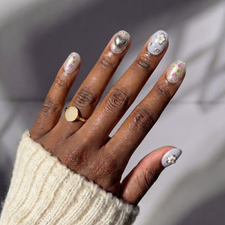Close up hand showcasing EyeCandys Fleur de Slay press on nails with blue glitter nails and silver floral rhinestone accents.