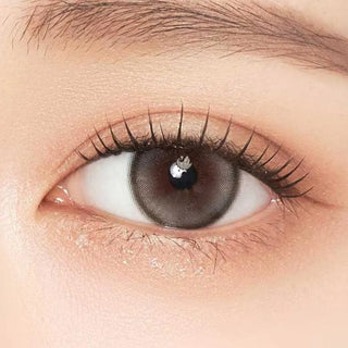 A close-up of an eye with long lashes and natural makeup, featuring Gemhour Demeter 1-Day 13.0 Pebble Grey contacts (10pk) that enhance the skin’s smooth, radiant look.