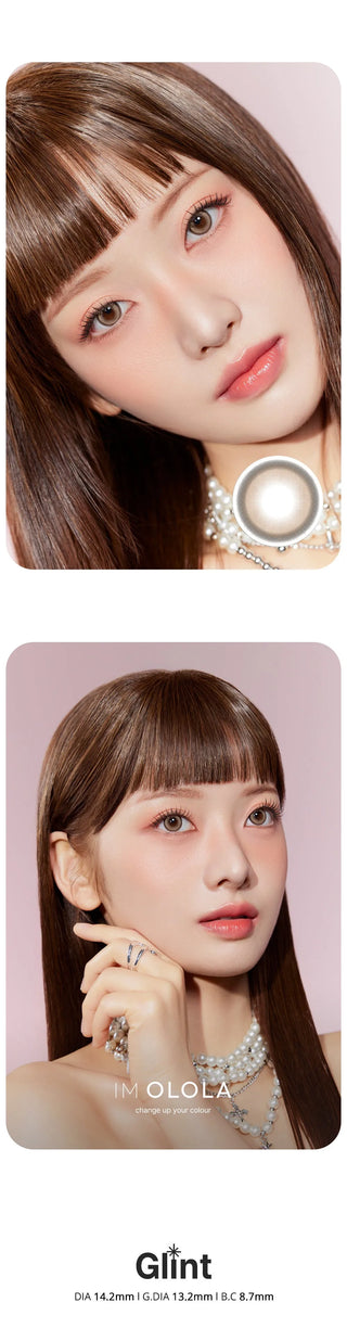 A woman with straight brown hair and bangs wears Olola Glint 1-Day Brown (10pk) lenses by Olola, pink makeup, pearl jewelry, and a white top, posing against a pale pink background. The word “Gift” appears at the bottom.