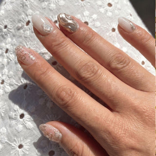 Close up hand showcasing EyeCandys Hanami press on nails with 3D floral texture, silver chrome nail, and elegant pearl accents.