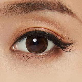 A close-up of a brown eye with long lashes, natural makeup, groomed brows, smooth light-toned skin, and NEO Vision Ruby Queen Brown (Custom Toric for Astigmatism) prescription colored contacts for a seamless look.