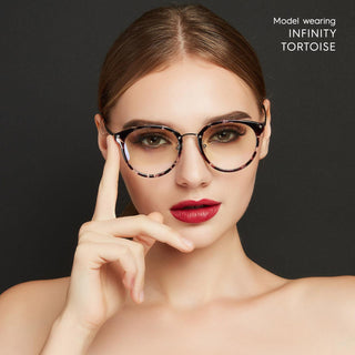 A woman with light skin and red lipstick wears EyeCandys Infinity Oversized Oval tortoiseshell eyeglasses, touching the frame with her finger. She poses against a black background, with "Model wearing Infinity Oversized Oval" in the top right corner.
