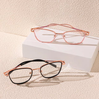 Two pairs of EyeCandys Kaylee Cat Eye eyeglasses with metal frames are displayed on a textured beige surface: one in pink on a white block and the other in black in front, showcasing chic fashion eyewear.