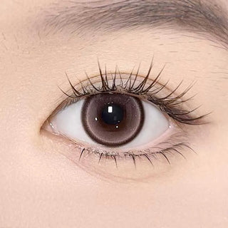 A close-up of a human eye with long lashes wearing Olola Meow Natural Angora Pink contacts by Olola, showing detailed iris texture and smooth, light skin around the eye.