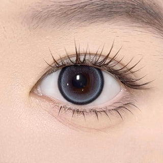 A close-up of a human eye with long lashes wears Olola Meow Natural Siam Blue contacts by Olola, making the iris look larger. Smooth, fair skin around the eye highlights the striking blue shade of these lenses.