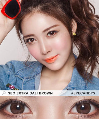 A young woman with wavy brown hair holds sunglasses, wearing orange lipstick, natural makeup, and NEO Vision Monthly Extra Dali Brown lenses. A close-up shows her brown eyes below. Text reads "NEO VISION EXTRA DALI BROWN #EYECANDYS.
