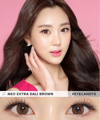 A woman with long, wavy dark hair poses against a pink background, wearing natural makeup and pink lipstick. A close-up highlights her brown eyes enhanced by NEO Vision Extra Dali Brown lenses. #EYECANDYS is displayed on the image.