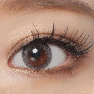 A close-up of a brown eye with long curled lashes, shimmery eyeshadow, and NEO Vision Monet Grey (Custom Toric for Astigmatism) lenses by NEO Vision, adding a subtle, captivating touch.