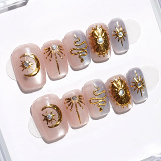 EyeCandys Nyx press on nails with sheer taupe lavender cat eye nails and gold celestial motifs including stars suns and abstract symbols.