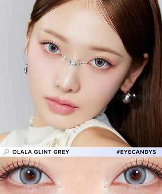 A woman with light makeup and rhinestone nose decor wears Olola Glint 1-Day Grey (10pk) contact lenses by Olola. A close-up highlights the grey color contacts. Text says “OLALA GLINT GREY” and “#EYECANDYS.”.