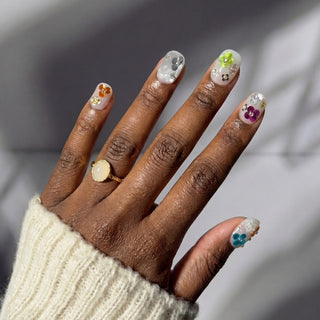 Close up hand showcasing EyeCandys Petal Rave press on nails with sheer jelly base, confetti sequins, and raised 3D flowers.