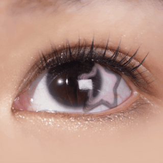 A close-up of a human eye with long lashes wearing EyeCandys Pink Star contacts by EyeCandys, shows a star-shaped reflection in the pupil and subtle shimmer on the eyelid.