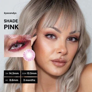 A woman with platinum blonde hair and pink eye makeup wears EyeCandys Shade Pink contacts, which give a natural champagne-pink look. Inset: close-up of lens (Diameter: 14.3mm, Graphic: 13.5mm, BC: 8.6mm). Lasts 3 months. Brand: EyeCandys.