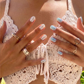 Hand wearing EyeCandys Plot Twist press on nails featuring mismatched design with iridescent white polka dot nails and blue jelly confetti nails.