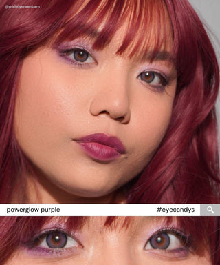 A woman with reddish-purple hair, purple eye makeup, and lipstick wears EyeCandys Powerglow Bluish Purple contact lenses. The close-up highlights her glowing skin and brown eyes. A zoom of her eyes reads: "EyeCandys Powerglow Purple #eyecandys.