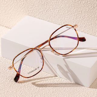 A pair of EyeCandys Farrow Round glasses with thin titanium frames sits on a white block against a textured light background, highlighting their classic vintage style.