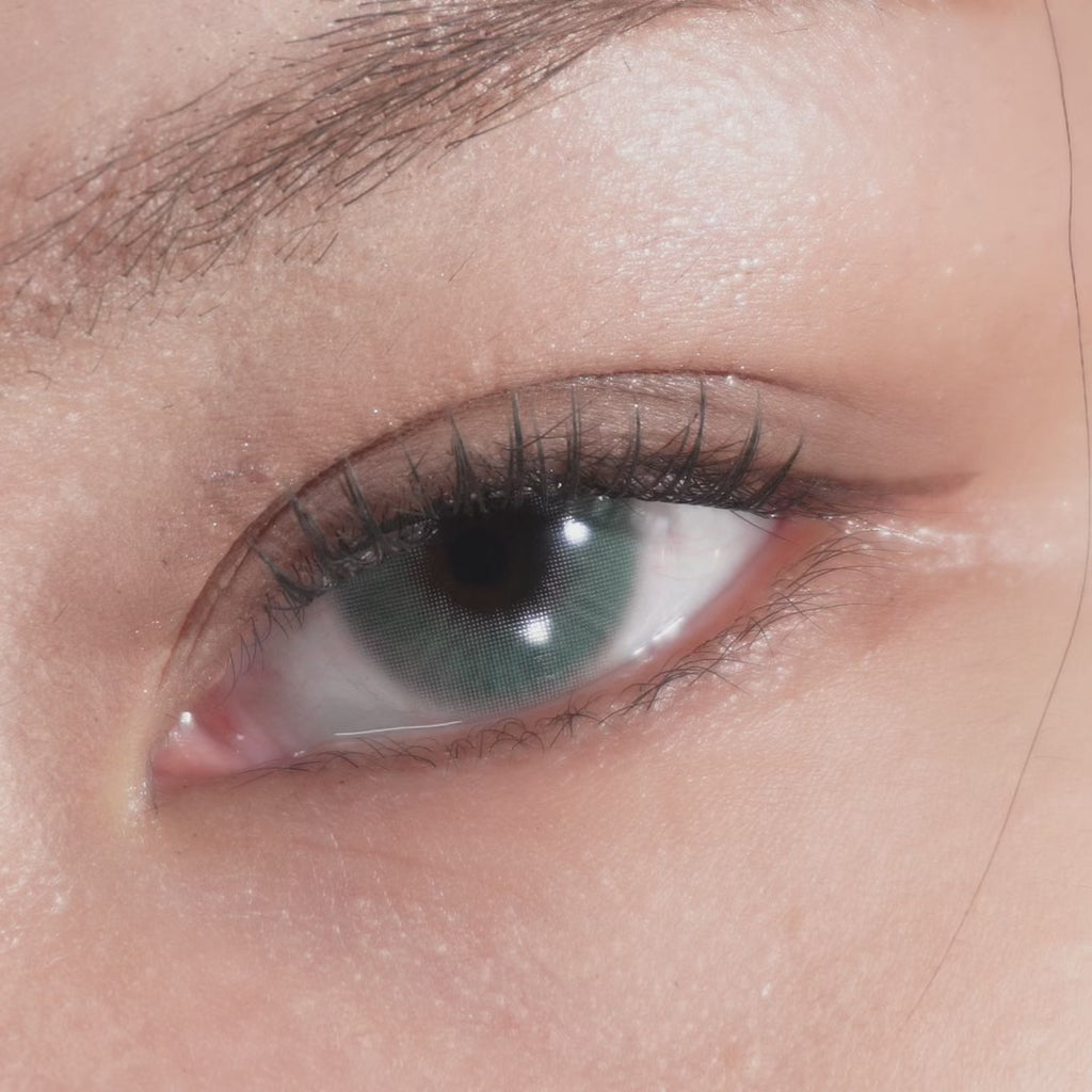 Close up of eye with long lashes blinking, wearing Eyecandys Aura Green Grey prescription colored contact lenses for a natural soft green-grey enhanced eye look
