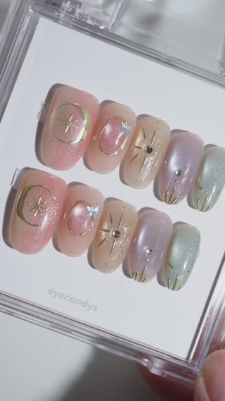 Wearing EyeCandys Star Script Press-On Nails — warm sunset cat-eye gradient in peach, blush, and muted gold with sculpted gold star and celestial motifs, short oval shape