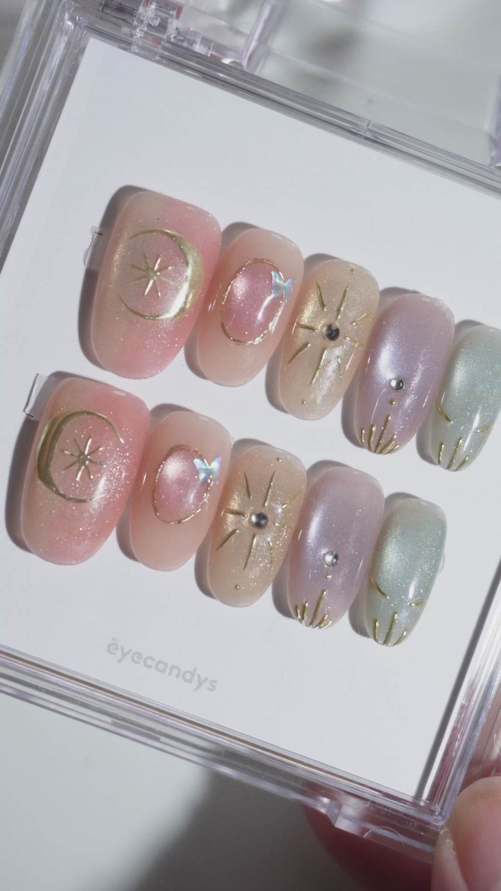 Wearing EyeCandys Star Script Press-On Nails — warm sunset cat-eye gradient in peach, blush, and muted gold with sculpted gold star and celestial motifs, short oval shape