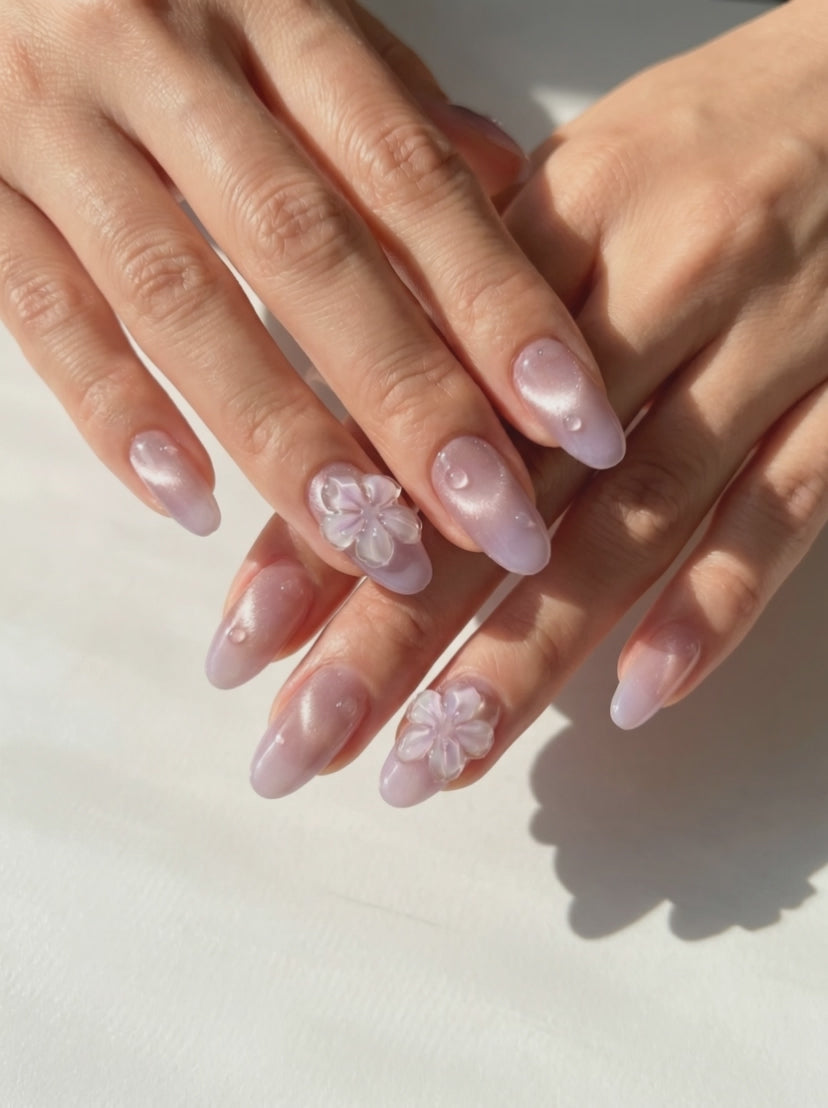Hand close-up showcasing EyeCandys Lilac Dew press-on nails featuring sculpted water droplet design and iridescent floral accent