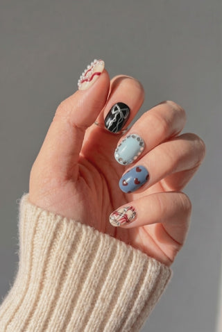 Wearing EyeCandys Heartbreak Hotel Press-On Nails, mismatched designs across cream, blue, plaid, black, and pearl-bordered nails in a short round shape