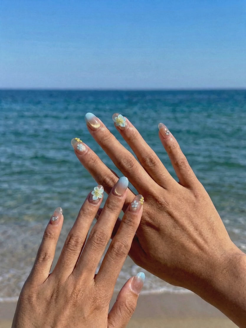 Wearing EyeCandys Lei'd Back Press-On Nails, sheer nude base graduating into soft gold shimmer with 3D plumeria flower accents in a short oval shape