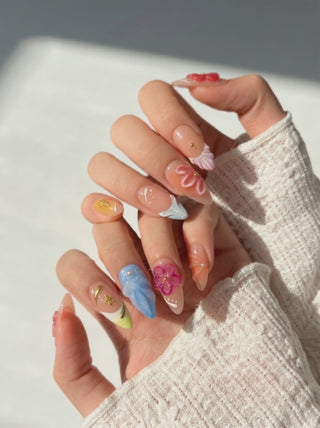 Wearing EyeCandys Flora Bora Press-On Nails, sheer nude base with colorful 3D floral designs, gold accents, and abstract patterns in an almond shape